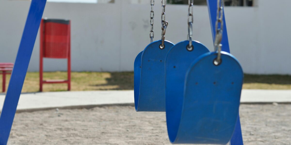 Blue swings in a sunny outdoor playground with sand and grass.
