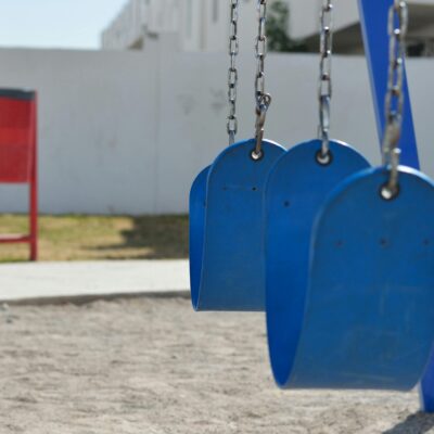Blue swings in a sunny outdoor playground with sand and grass.